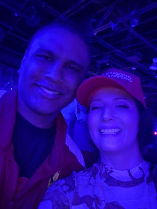 A man and woman pose for a selfie under blue nightclub lighting, with the man wearing a red cap that reads "TRUMP 2024 KEEPING AMERICA" as he references himself as "Franklin the pump.fun guy."