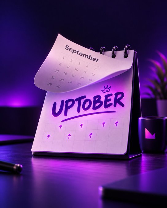 A purple-themed digital rendering of a spiral-bound flip calendar displaying 'September' on the top page and 'UPTOBER' with upward arrows on the page below, sitting on a desk next to a dark mug and a plant.