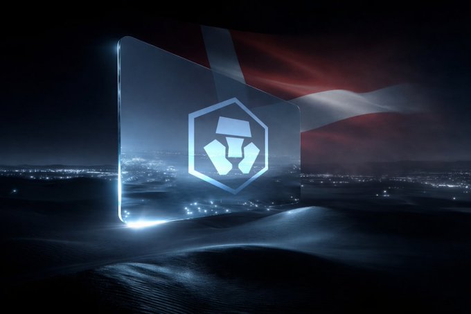 A dark, stylized digital illustration shows a glowing Crypto.com logo on a card floating above a desert landscape, with the red and white flag of Latvia waving in the background.