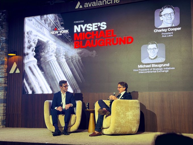 Two men in suits seated in yellow chairs on a stage during a 'FIRESIDE NYSE'S MICHAEL BLAUGRUND' event sponsored by Avalanche, with a screen showing photos of Charley Cooper (President, Ava Labs) and Michael Blaugrund (Vice President of Strategic Initiatives, Intercontinental Exchange).