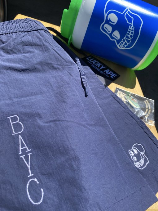 A display of merchandise from "LUCKY APE" featuring a blue garment with "BAY C" embroidered on it, alongside a blue and green water bottle branded with a monkey skull logo.
