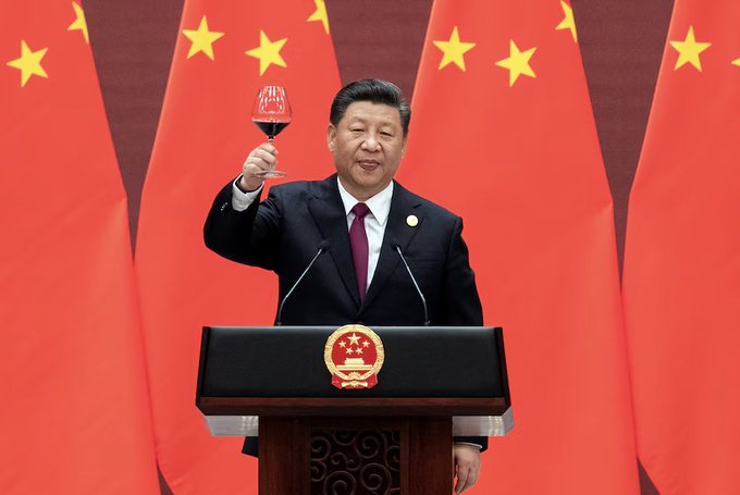The image shows a man standing at a podium holding up a glass of wine while giving a speech. He appears to be addressing an audience or delivering a message, possibly related to China's economy or financial matters. The background features red Chinese flags, which could symbolize national pride and unity. Additionally, there is text in the image that reads "CHINA BANNED CRYPTO. BITCOIN JUST GOT IN ANYWAY. You can now send money to China in seconds. Settled on Bitcoin. Lightspark opened the corridor to all its customers." This suggests that the man at the podium might be discussing the recent ban of cryptocurrency, particularly Bitcoin, in China and how it affects the country's economy or financial landscape.