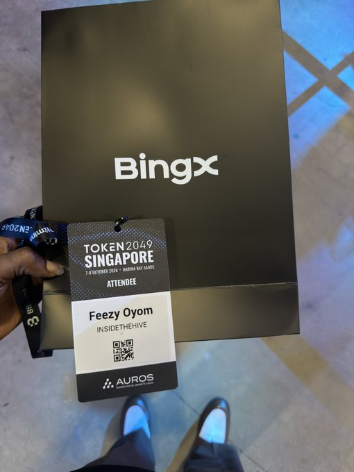 A hand holds a "Token2049 Singapore" attendee badge (1-3 October 2024, Marina Bay Sands) for "Feezy Oyom" from "InsideTheHive," displayed in front of a black BingX-branded box, capturing a Token2049 networking moment.