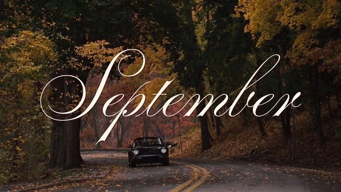 The word "September" written in elegant cursive script over an autumn forest scene with a car driving down a winding road.