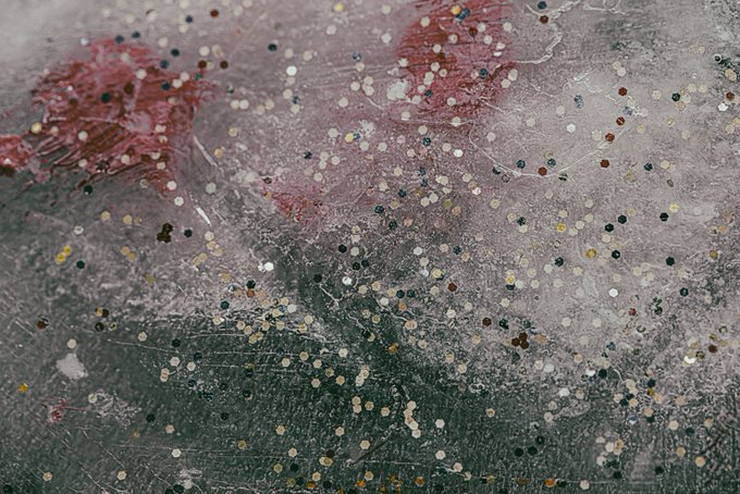 A textured abstract artwork with a speckled pattern of dots in various colors over a background of muted pink, gray, and dark green tones.
