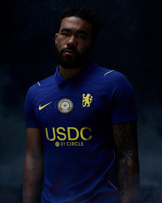 A man models Chelsea FC's new blue kit featuring the Nike logo, club crest, and a prominent yellow "USDC BY CIRCLE" sponsor patch, marking the crypto firm's debut on the team's jersey.