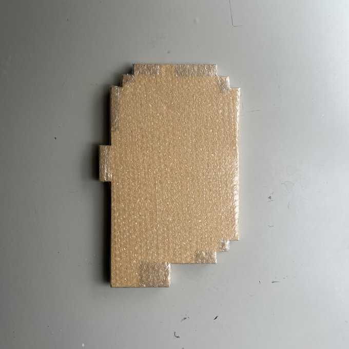 A rectangular piece of beige foam with a stepped, irregular shape rests on a plain light gray surface.