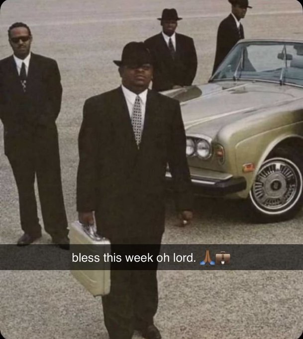 A man in a black suit and fedora leads a group of similarly dressed men beside a luxury car, with overlaid text reading "bless this week oh lord. 🙏🪑" The image conveys a confident, powerful "boss" energy that matches the post's motivational message wishing followers a productive new week.
