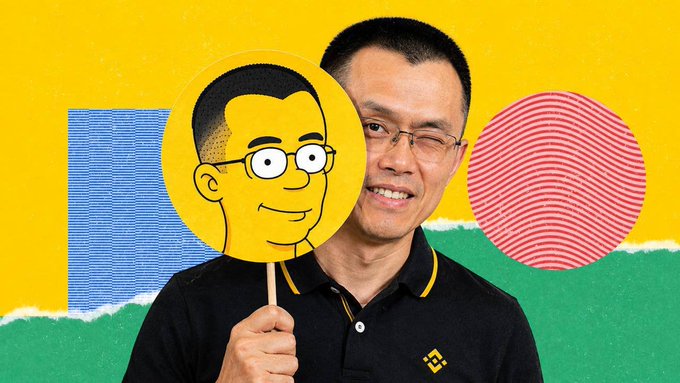 An Asian man smiling while holding up a cartoonish yellow sign of a face with glasses, set against a vibrant yellow, blue, and green background featuring a red fingerprint-like circle.