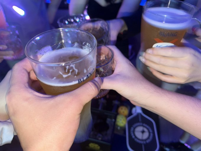Multiple hands clinking together glasses of beer branded with 'BLANC' in what appears to be a nightclub or bar setting.