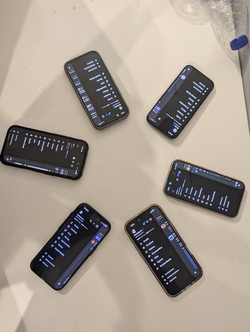 Six smartphones are arranged in a circle on a white table, all displaying what appears to be chat or messaging interfaces, with a water bottle visible in the upper right corner—visually representing the in-person meetup with the top builders in Abuja referenced in the post.