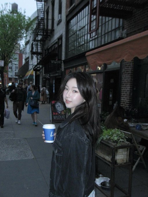 A young woman holding a coffee cup stands on a city street in front of a 'WILDLIFE' storefront.