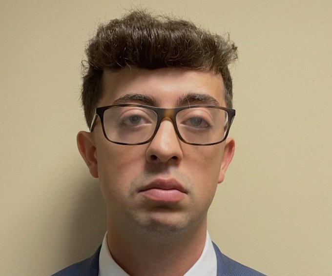 A young man with tousled dark hair and tortoiseshell glasses poses against a beige wall, his neutral expression captured in what appears to be a formal portrait — fitting for the playful "Pablo Pledgescobar" caption, which humorously grafts a cartel-scion moniker onto his serious, scholarly appearance.
