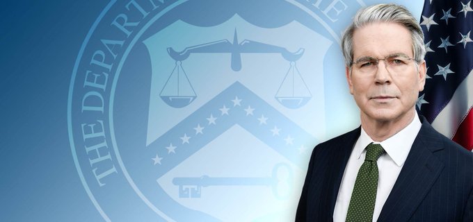 Scott Bessent, the U.S. Secretary of the Treasury, is pictured in front of the Department of the Treasury seal and an American flag, visually accompanying news of the Treasury's proposed regulations implementing the GENIUS Act for payment stablecoins.

Key visible text: "THE DEPARTM..." (partial text from the Department of the Treasury seal).