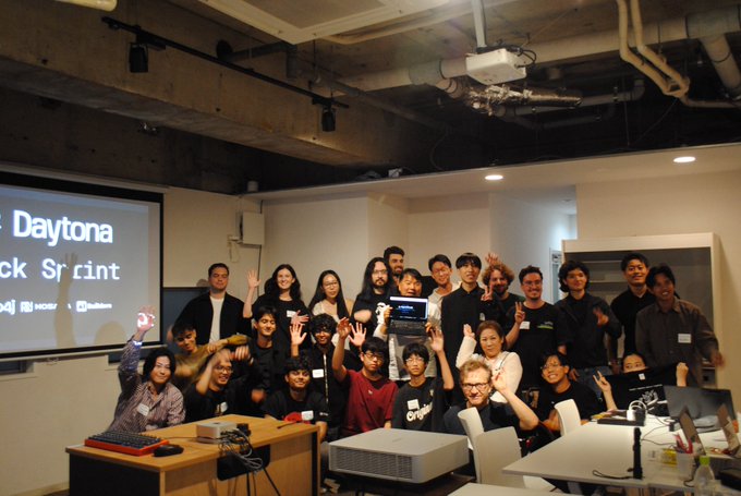A group photo of attendees at a "Daytona Hack Sprint" event, posing with raised hands and holding up a small award.