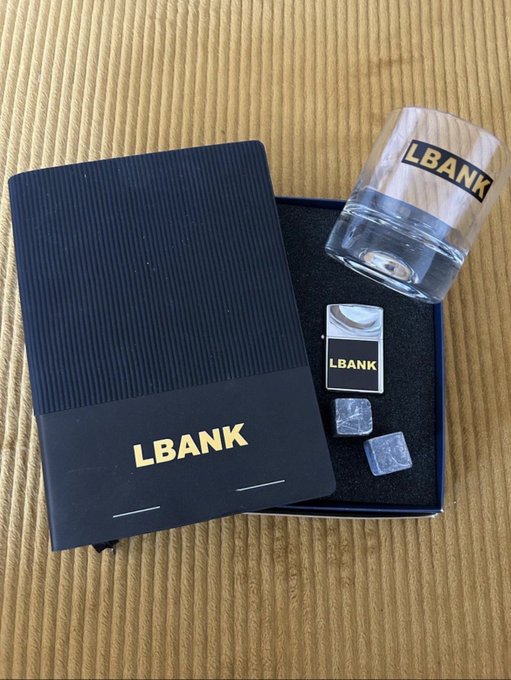 The image features an open notebook laying flat on its side, along with a glass of water and a small black box containing a keychain and some other items. The text "May our new collaboration be blessed" can also be seen in the image.
