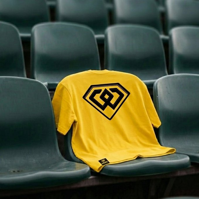 A yellow t-shirt with a black diamond-shaped logo draped over a green stadium seat in an empty arena.