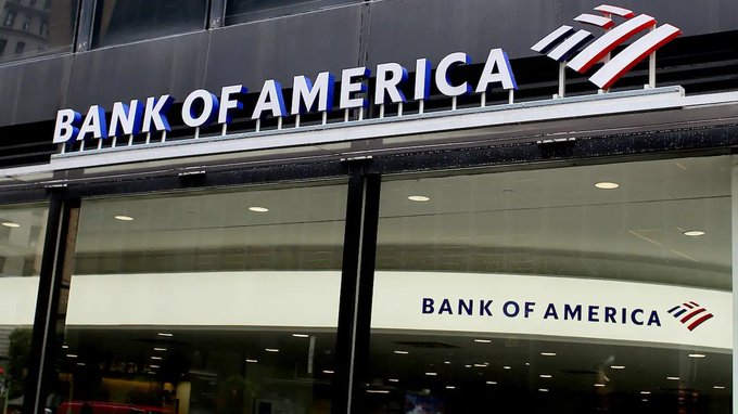 The image shows the exterior of a Bank of America branch with the company's logo and name prominently displayed on signage above and beside the entrance. It visually reinforces the article's point that Bank of America ($BAC) is among major U.S. financial institutions collaborating on a new stablecoin initiative alongside other major banks like Citigroup, Goldman Sachs, and Wells Fargo.