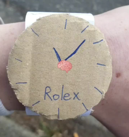 A handmade circular cardboard Rolex watch with "Rolex" written on the dial, held up on someone's wrist—the context suggesting it was a humorous prize or novelty item won from a Pump.fun gacha game.