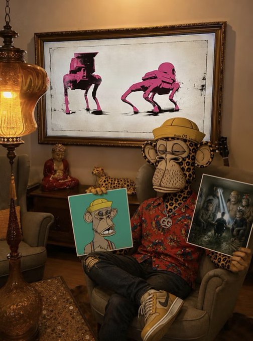 A Bored Ape NFT character wearing a yellow cap, glasses, and a red floral shirt sits in an armchair holding a print of its own portrait, with a star wars themed print in the other hand, in a room with a Buddha statue and pink art.