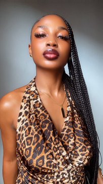 A woman with long braids wearing a leopard-print halter dress poses for a portrait against a gray background.