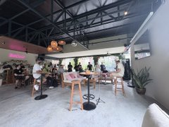 A modern cafe or co-working space with patrons seated at tables, featuring exposed ceiling beams and a bar area.