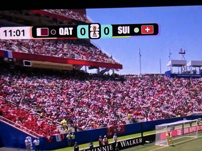 The image shows a large stadium filled with spectators, where two soccer teams are playing against each other. A scoreboard can be seen above the field displaying the scores of the match. The crowd appears to be engaged in watching the game, creating an atmosphere of excitement and anticipation. The focus on the scoreboard and the players' positions suggests that this is a competitive match between the two teams.