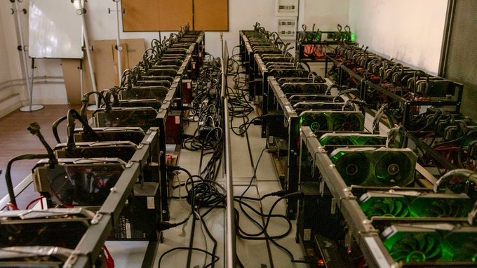 Rows of cryptocurrency mining rigs with glowing green LED fans are set up in a warehouse, illustrating the equipment used in BitClub Network's alleged $722 million crypto mining fraud orchestrated by its founder Matthew Goettsche.
