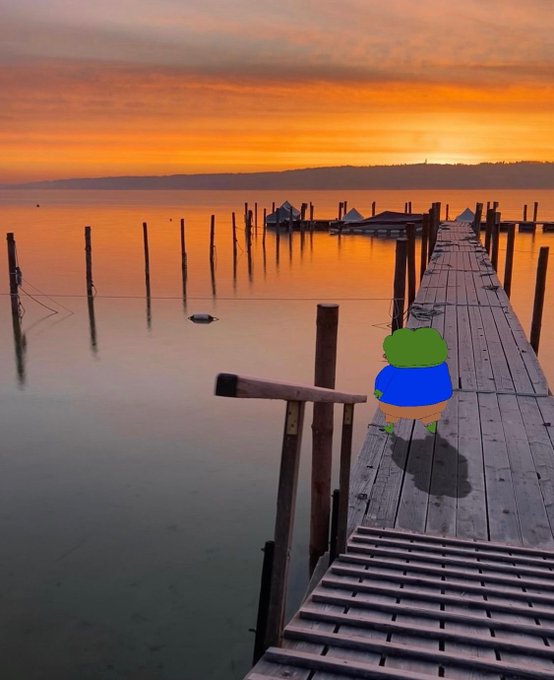 A serene sunset over calm water features a wooden pier extending into the lake, with a small cartoon frog character standing on the walkway.