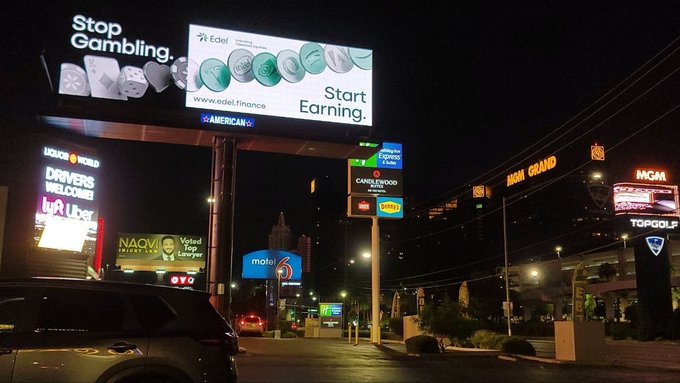 The image shows an urban street scene at night with a billboard advertising a casino game called "Start earning". The billboard is located near a parking lot where several cars are parked, including one car that appears to be a truck. In addition to the billboard, there are also other signs and advertisements visible in the area.