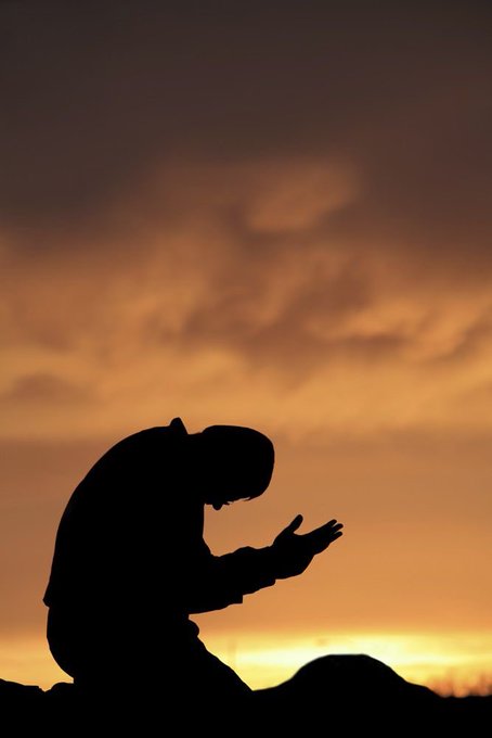 A silhouette of a praying person with pointed ears set against a dramatic orange sunset sky.