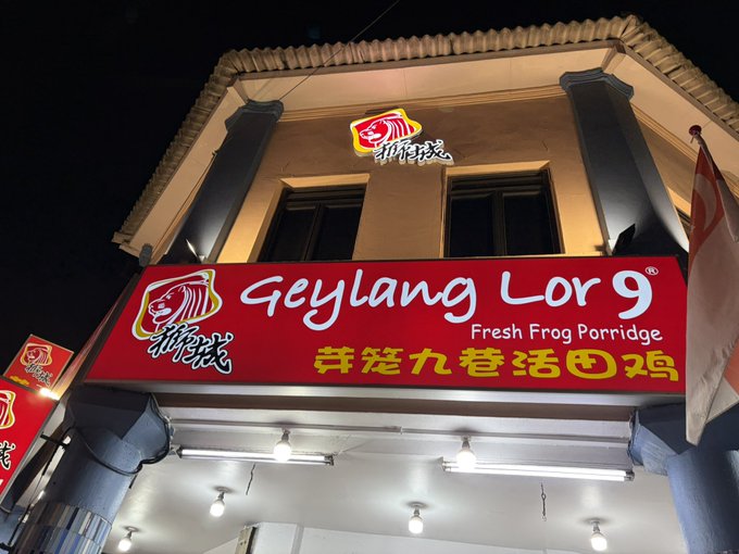 Nighttime photo of a "Geylang Lor 9 Fresh Frog Porridge" restaurant sign with its distinctive red logo featuring a frog, displayed in both English and Chinese (芽笼九巷活田鸡) on a red storefront.