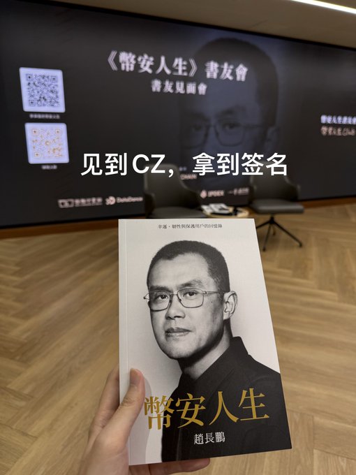 A hand holding a Chinese book titled '幣安人生' (Binance Life) by 趙長鵬 (CZ), with Chinese text overlay reading '见到CZ，拿到签名' (Met CZ, got signature), taken at a book signing event.