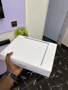 A hand displays a white "MacBook Pro" box on a dark marble surface, with the caption playfully suggesting the laptop represents proof of cashing out profits from the 2026 bull market.