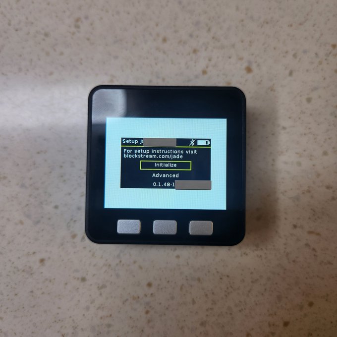 A Blockstream Jade hardware wallet displaying a setup menu with the prompt 'For setup instructions visit blockstream.com/jade' and options to Initialize, Advanced, or view version 0.1.40-1.