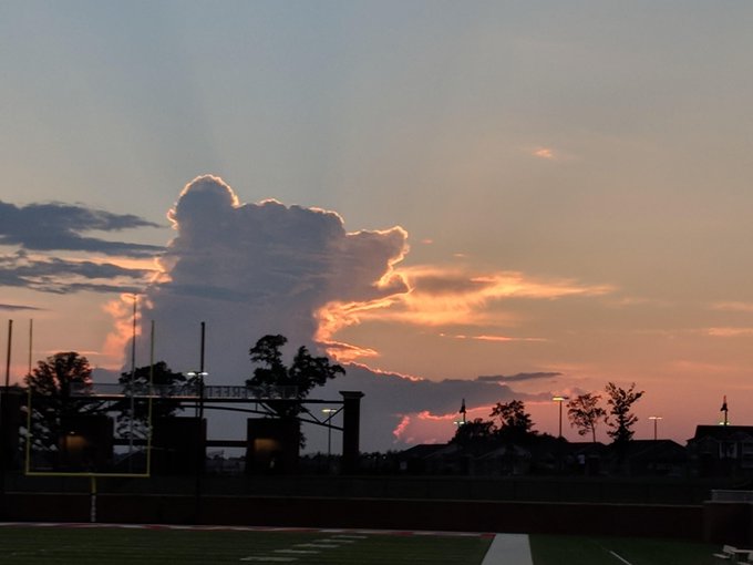 A dramatic sunset over a football field features a massive cloud formation shaped like a bull charging forward, its golden-pink silhouette matching the accompanying "#BTC" post's bullish sentiment as a visual "sign" pointing toward Bitcoin's upward momentum.