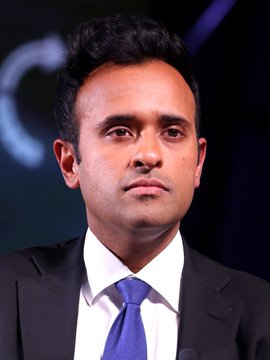 A man in a dark suit with a blue tie appears serious at what looks like a formal event or interview setting. The image likely accompanies news about Vivek Ramaswamy, whose company Strive has been aggressively accumulating Bitcoin, now holding 24,531 BTC worth over $1.9 billion.