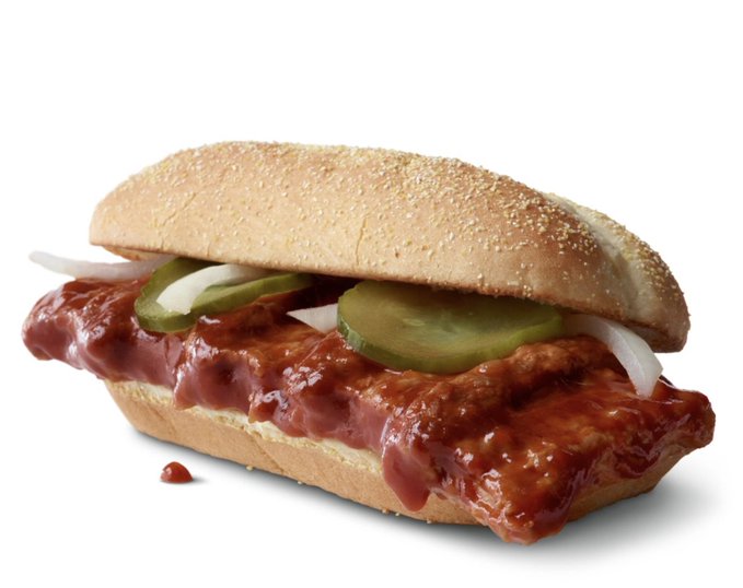 A barbecue-sauced hot dog in a sesame seed bun, topped with pickle slices and onions. The accompanying post says “aped,” matching the informal food caption vibe.