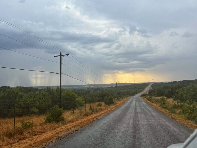 A two-lane country road stretches into the distance beneath a dramatic, cloudy sky with rays of sunlight breaking through near the horizon, flanked by utility poles and rolling green terrain.

The image reflects the peaceful, winding-down mood of the post—perfect for an evening walk and quiet reflection, with the open road and softening sunset light evoking a sense of calm and unwinding after the day.