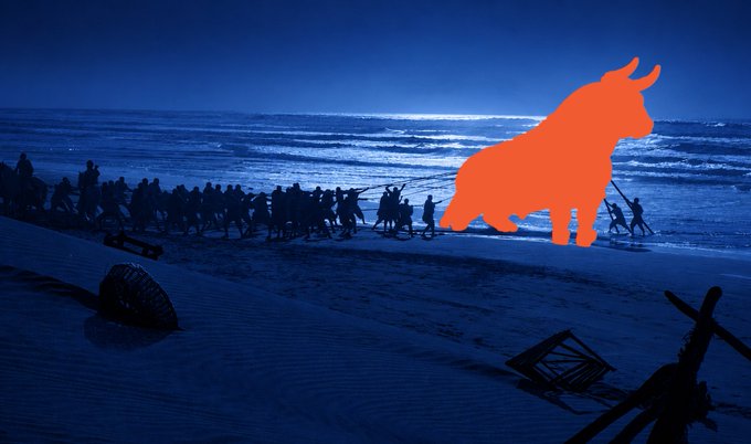 A dark, silhouetted beach scene at dusk or dawn with a large, bright orange bull shape digitally overlaid on the image, appearing to charge across the sand.