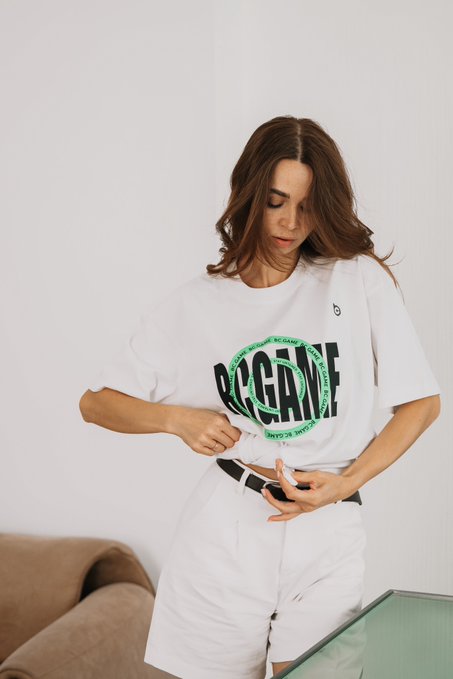 A woman wearing a white t-shirt with a green circular 'NO GAME' graphic and white shorts, adjusting her clothing.