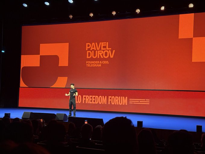Pavel Durov, Founder & CEO of Telegram, stands on stage delivering a presentation at the Oslo Freedom Forum, with his name and title displayed prominently on the large orange screen behind him, embodying the post's theme of a "Digital Freedom of Speech Fighter."