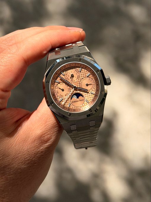 A hand holds an Audemars Piguet Royal Oak Perpetual Calendar with a salmon-colored dial, showcasing its moon phase complication, sub-dials for day/date, and "AUDEMARS PIGUET AUTOMATIC" text on the face—representing the "Salmon Perp ltd 300" piece mentioned in the thread.