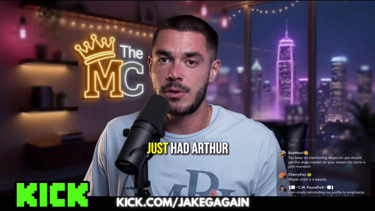 The image features a man wearing a white shirt, standing behind a microphone with a microphone stand. The background of the image shows a city skyline at night, which adds an urban atmosphere to the scene. The caption for the image reads "Jake gives us his TOP 3 memecoins he'S holding this cycle. 
The trilogy of memecoins this cycle is $UTYA on $TON UTM on $WOJAK on $ETH & $TROLL on $SOL".