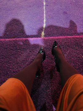 A person wearing an orange outfit and stiletto heels stands on a purple carpet bathed in neon light, casting distinct heel-shaped shadows against the wall. The image playfully supports the "proof of church" caption by suggesting the heel shadows resemble a cathedral-like silhouette.