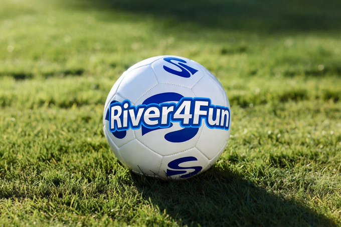 The image features a soccer ball sitting on top of a grassy field, with the words "River4Fun" written on it. The background of the image shows a green field, which further emphasizes the focus on the soccer ball. The text "@RiverdotInc Combining football (community, fun, global)" and "@River4fun" are also present in the image. This combination of elements suggests that the image is promoting the idea of combining sports with cryptocurrency or blockchain technology to create a more engaging and interactive experience for users.