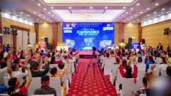 The image shows a press conference or official meeting in a large hall, with attendees seated facing a stage featuring a blue banner with Vietnamese text, though no specific names or numbers are clearly visible. The setting likely relates to the Thai Nguyen Provincial Police's announcement about dismantling the cryptocurrency ring, with officials possibly addressing the 3,000 victims and the 100 billion VND in damages from the "CVX digital currency" scam.