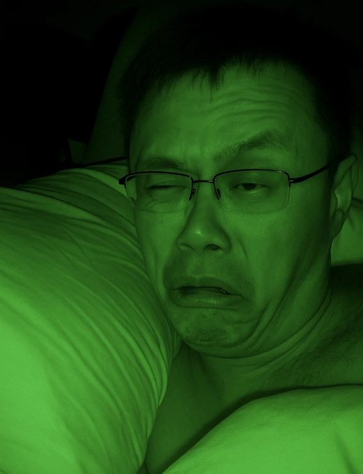 A man with glasses lies on a pillow with a tired, weary expression, bathed in eerie green light that gives the scene a sickly, unwell appearance—visually echoing the post's reference to "TCC was Right!" as if validating some grim prediction with his exhausted, haggard look.