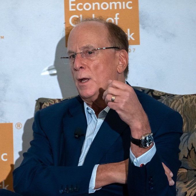 An older man with glasses and a blue blazer speaks at what appears to be an Economic Club event, gesturing with his hand.
