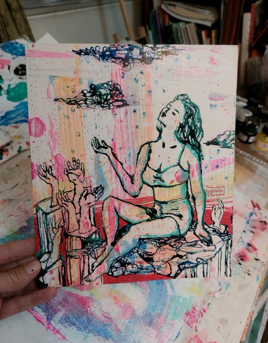 A mixed-media artwork held in someone's hand depicts a seated nude female figure surrounded by smaller hands and chaotic scribbles in pink, blue, and green tones.